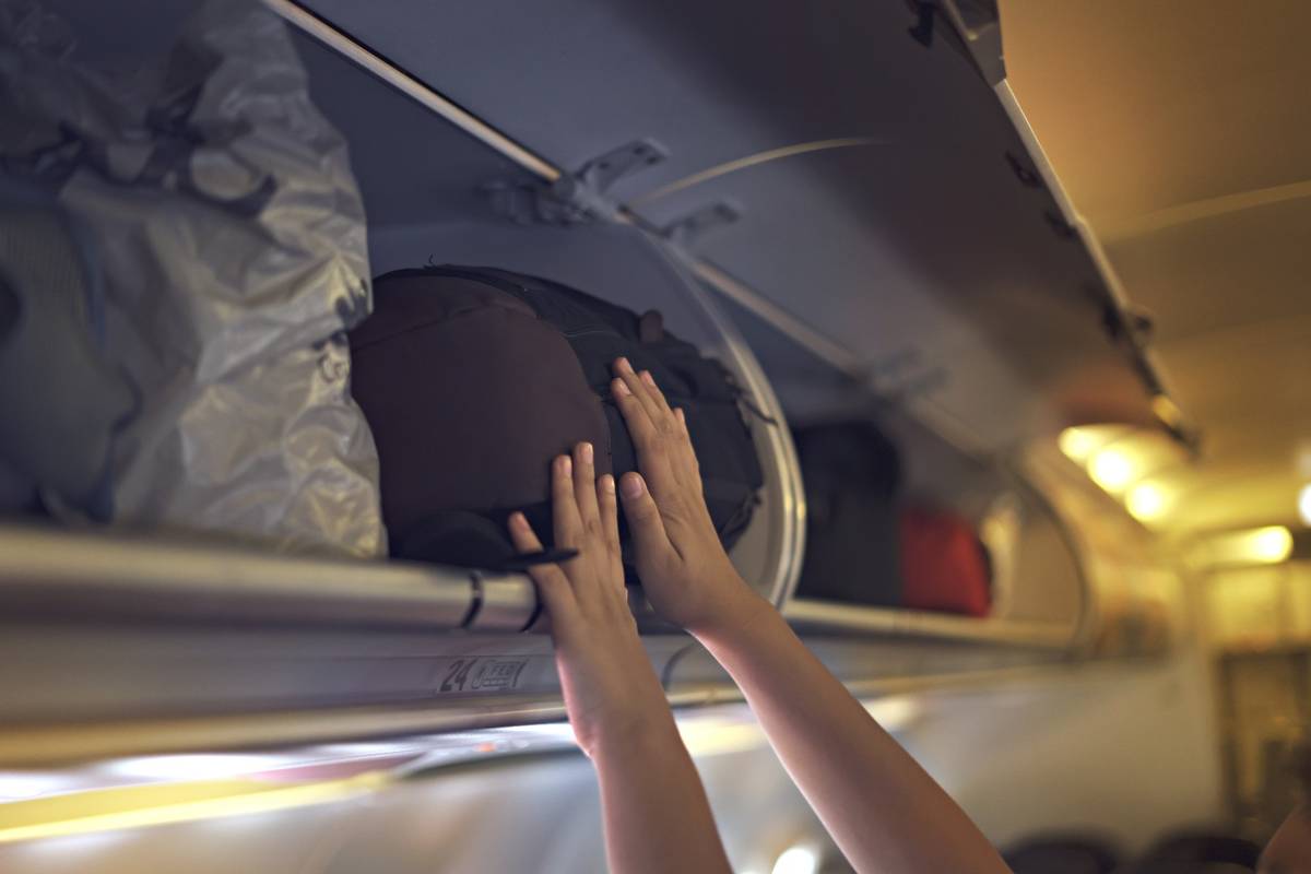Someone putting luggage in an airplane's overhead bin