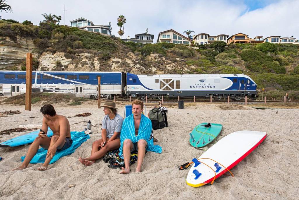 Des gens assis sur la plage avec un train Amtrak derrière eux.