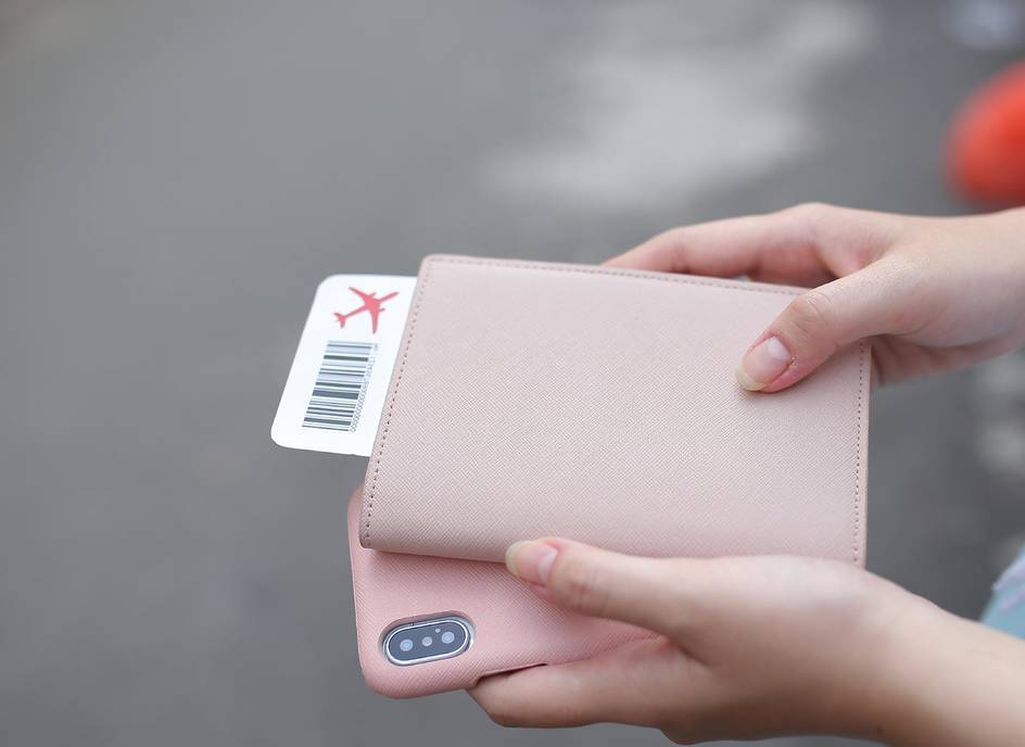 A woman holding her plane ticket, cellphone and a passport case