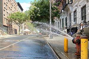 New York, NY USA - July 23, 2021 : Man sitting on apartment building stoop in front of a traffic-free Open Street with an open fire hydrant in the summer in Washington Heights, New York City