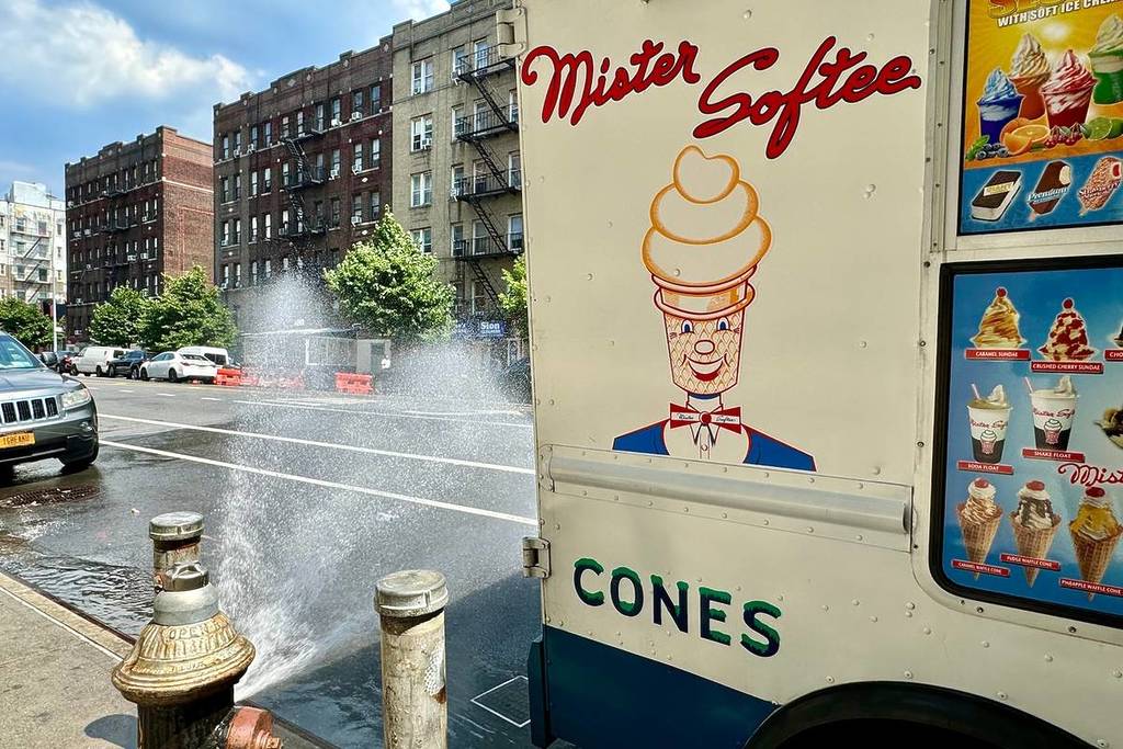 New York, NY USA - June 21, 2024 : Open fire hydrant spraying water behind a Mister Softee ice cream truck in Washington Heights, Manhattan, New York City