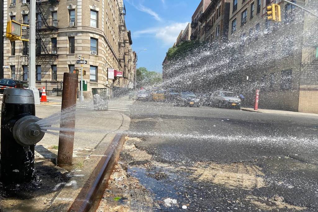 Zicht op een open brandkraan met dop die water op straat spuit op een hete zomerdag in New York, NY, VS