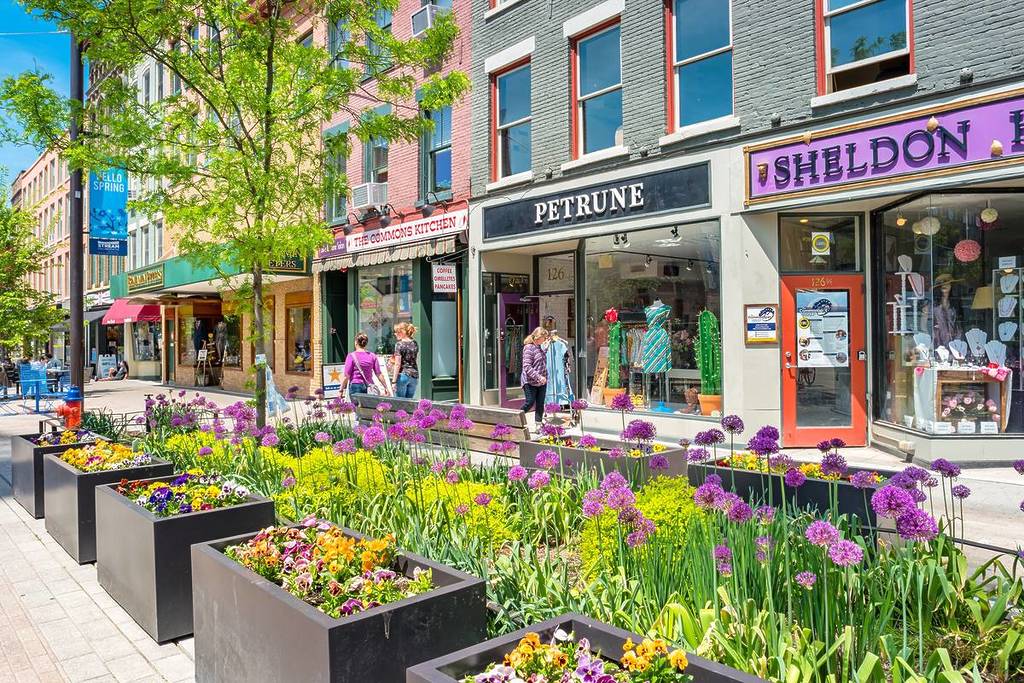 En un día soleado, la gente pasa junto a coloridas tiendas en una zona peatonal del centro de Ithaca, en el estado de Nueva York (EE UU).
