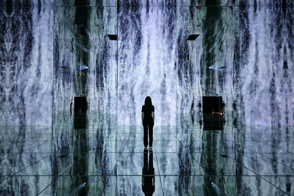 Donna in piedi di fronte all'imponente cascata digitale WATERFALL INFINITE all'Arte Museum New York presso Chelsea Piers