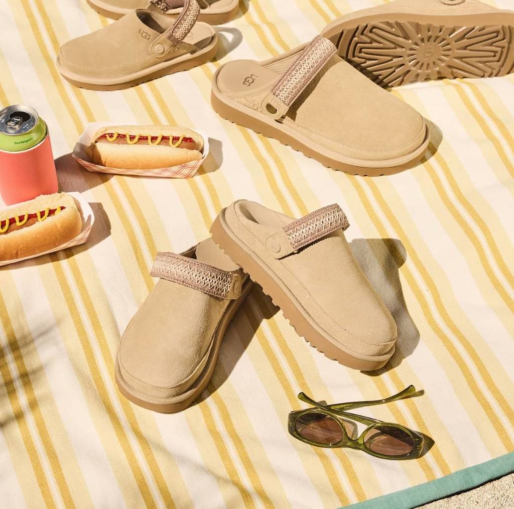 Several pairs of UGG Mustard Seed clogs on a picnic rug with free hot dogs, a can of drink and sunglasses.