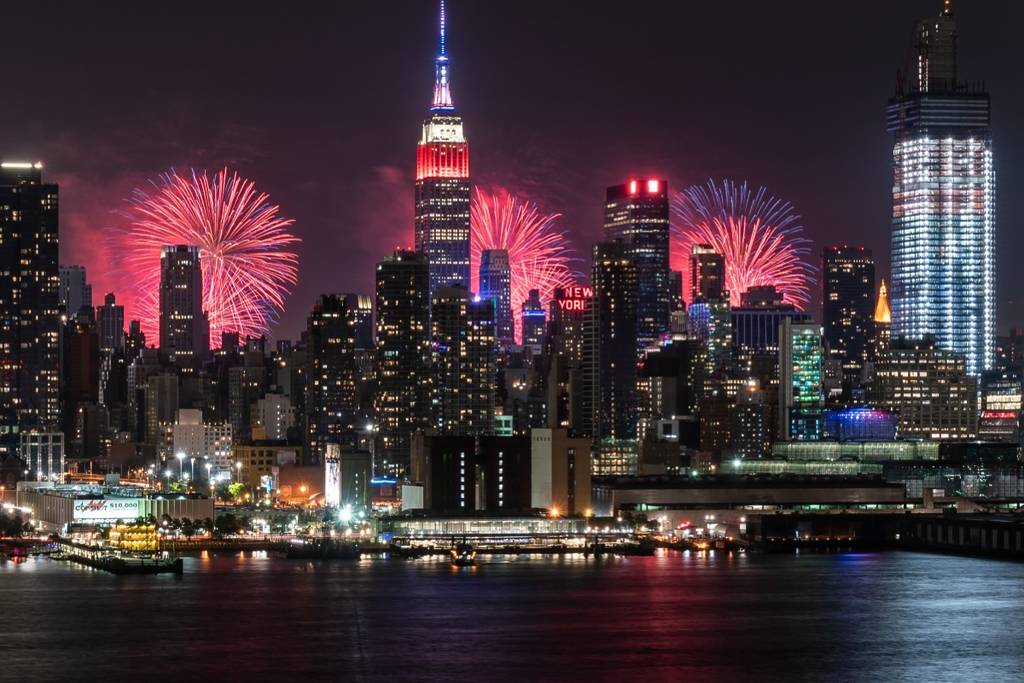 Empire State Building rood, wit en blauw verlicht voor de vierde juli met vuurwerk op de achtergrond