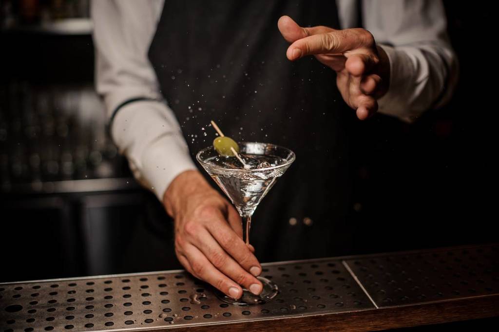 Bartender preparando um coquetel de verão de martini fresco e forte com uma azeitona verde e sal