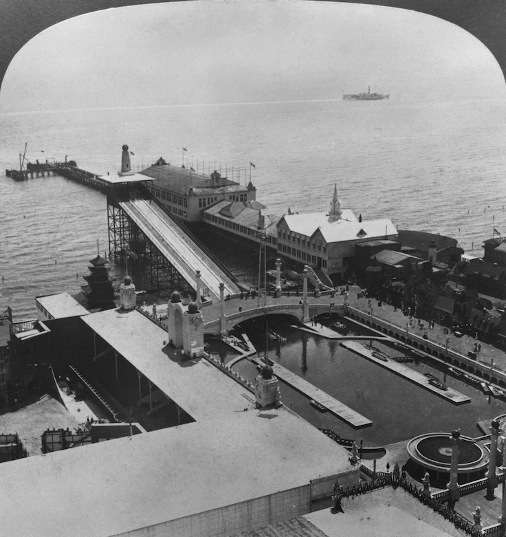 A high-angle view of the 'Dreamland' amusement park, showing the 'Flame City' attraction (left), the 'Shoot the Chutes' attraction (centre), and the Dancing Pavilion on the pier (right), on Coney Island in the borough of Brooklyn, New York City, New York, circa 1904. The image is one-half of a stereoscopic image. (Photo by H. C. White/Archive Photos/Getty Images)