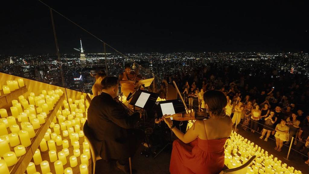 A string quartet plays among 1000s of candles on top of Edge with a view of the NYC behind.