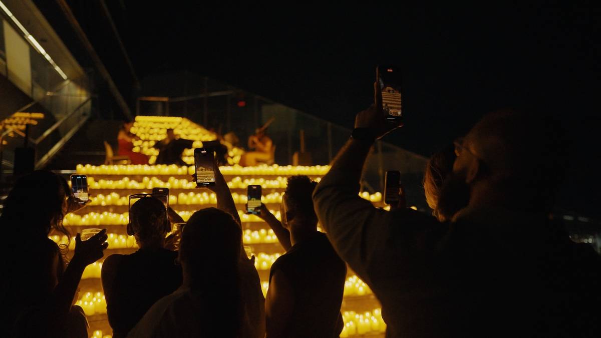 A crowd of people take photos of a string quartet playing on the steps of Edge surrounded by 1000s of candles.