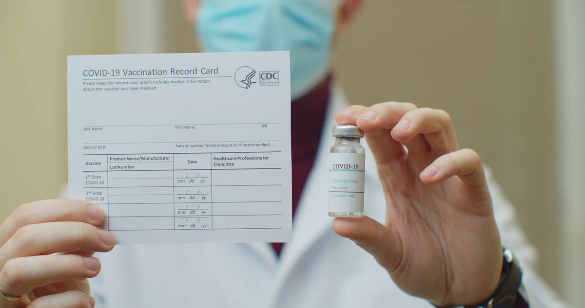 Doctor holding Covid vaccine card and vaccine bottle