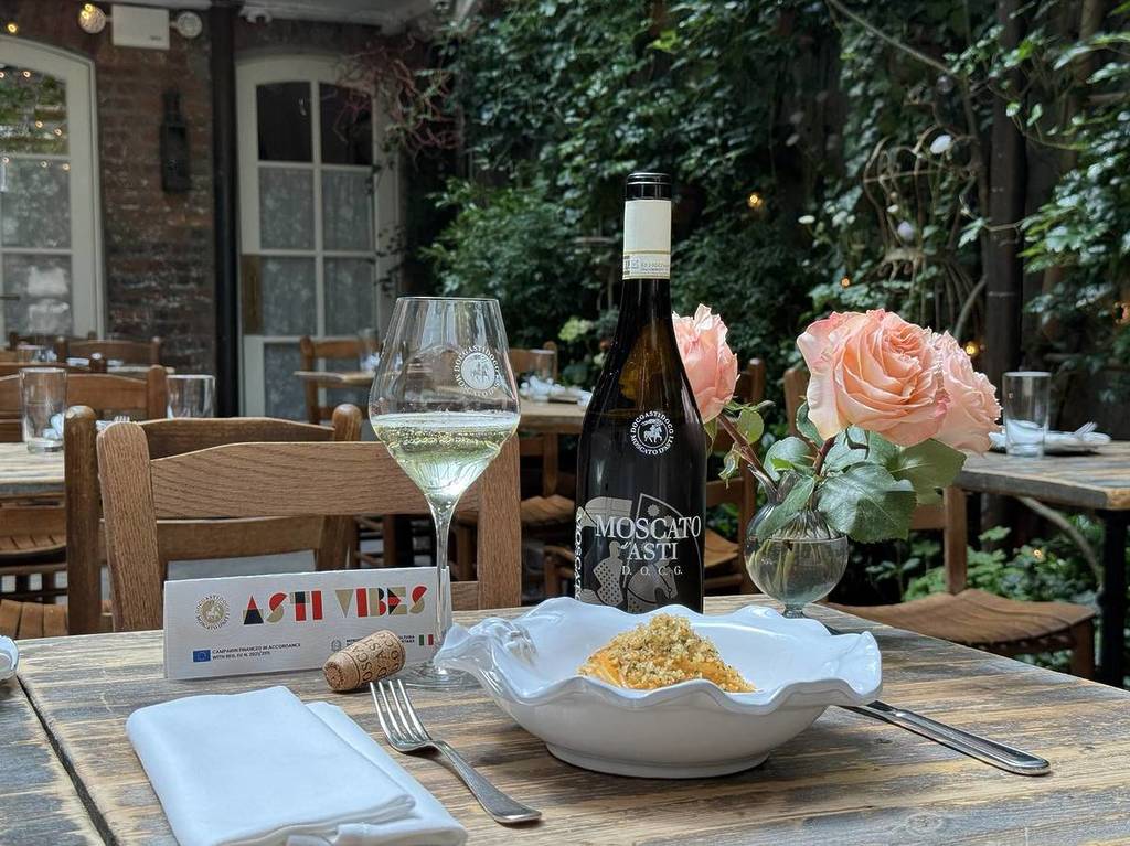 A bottle of Moscato d'Asti DOCG sits on a table in the Palma courtyard with a pasta dish.
