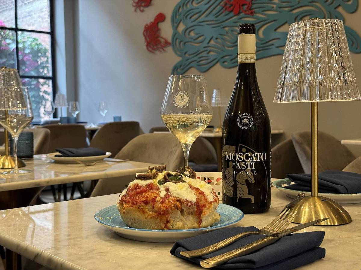 A bottle of Moscato d'Asti DOCG sits on a table at Amo with a filled glass next to it and a foccacia dish.
