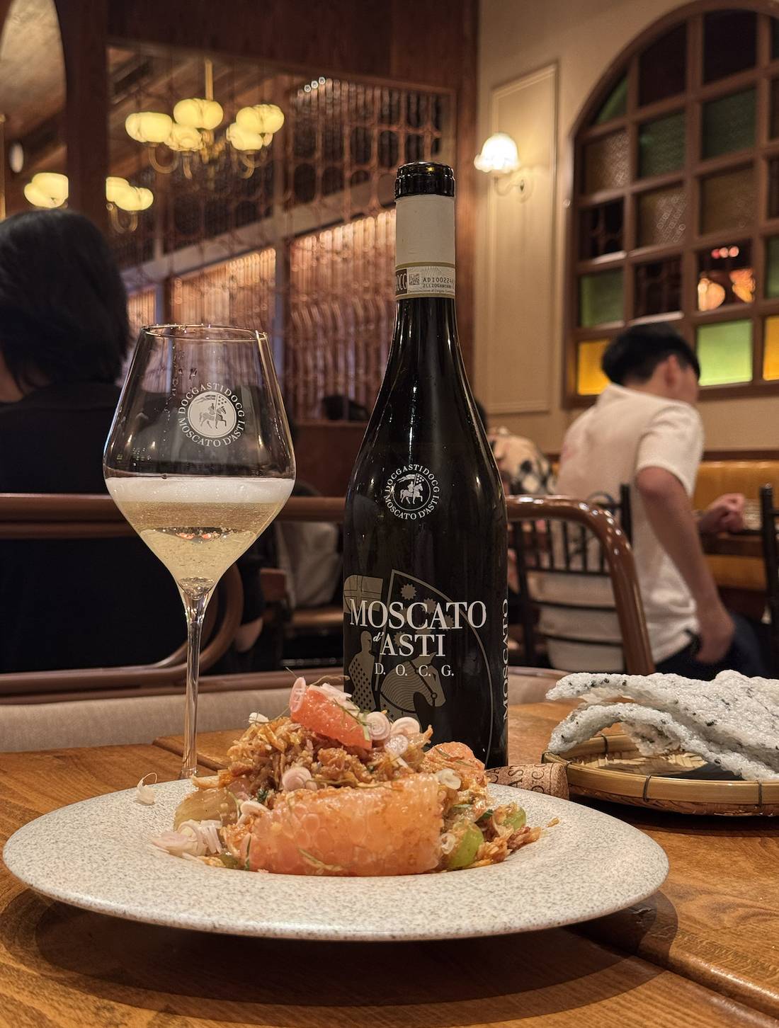 A bottle of Moscato d'Asti DOCG sits alongside a filled glass and a dish from La Dong.