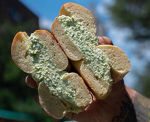 person holding a bagel cut in half with green cream cheese from Brooklyn Bagel and Coffee Company
