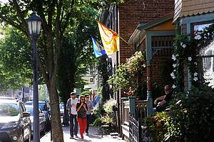 Lambertville, USA - September 15, 2013. People walking on sidewalk eating ice creams with a man sitting on porch in Lambertville, New Jersey. Lambertville is a historic town in the Hunterdon County of New Jersey. It is located on the east bank of scenic Delaware River and attacts visitors with antiques shops, art galleries and restaurants. Its streets are lined with elegant well-preserved federal townhouses and Victorian homes.