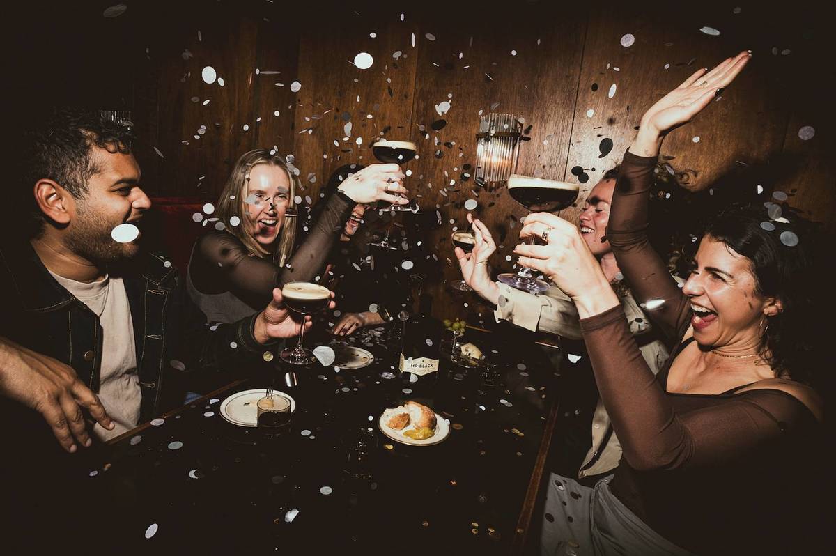 People enjoying Espresso Martinis with confetti flying around at a table.