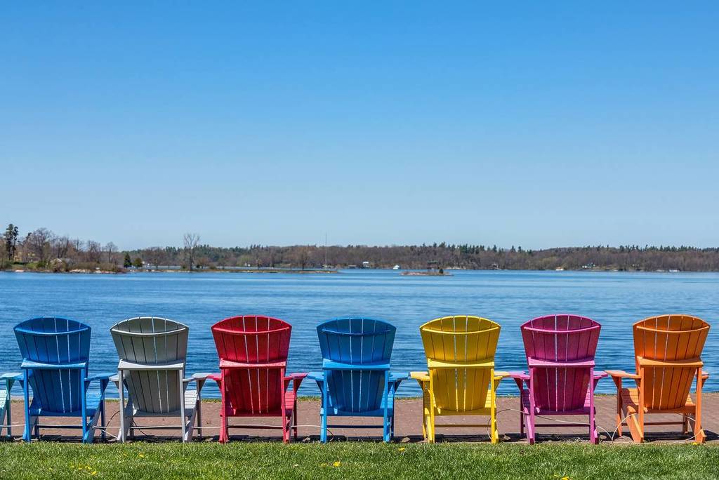Clayton, NY/USA - May 2016: A row of colorful Adirondack chairs are lined up along the waterfront on the St. Lawrence River so visitors can watch large ships as they pass headed to the Great Lakes.