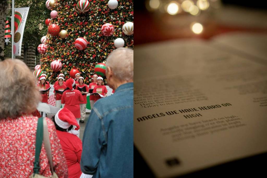 A group of people watching carolers singing in front of a Christmas tree