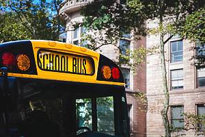 A close up of the front end of a traditional American yellow school bus with large sign and safety lights in a city environment