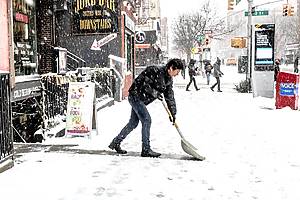 Man shoveling snow in front of his business in nyc