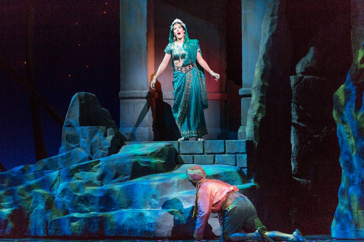 An opera singer performing on stage at an opera show as a male performer is on his knees