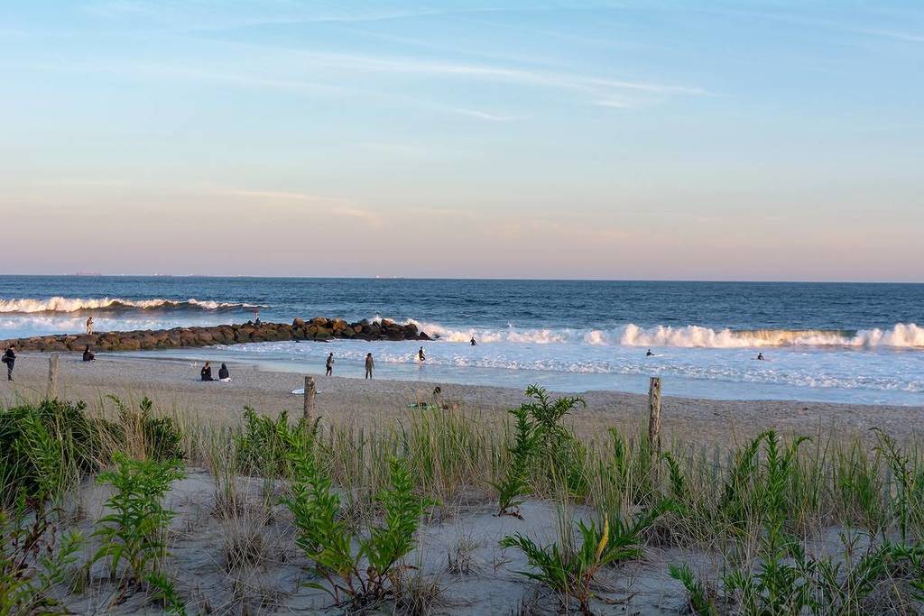 Blick über eine Sanddüne von der Promenade am Rockaway Beach in der Nähe der Beach 67th Street bei Sonnenuntergang