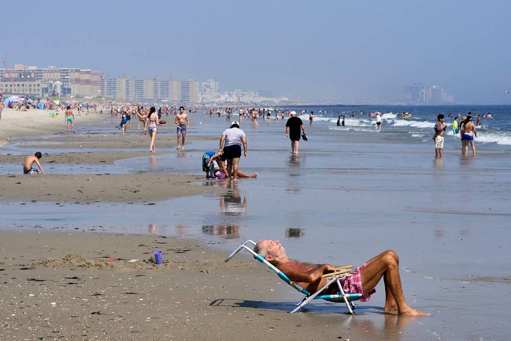 Queens, NY – 26. August 2021: Strandbesucher genießen an einem heißen Sommertag Sonne, Sand und Brandung am Rockaway Beach in Queens, NYC. Ein Mann sitzt auf einem Liegestuhl am Wasserrand. 