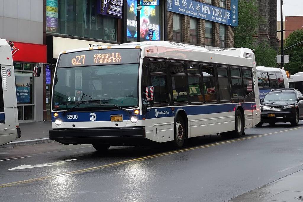 Um ônibus local Q27 com destino à Springfield Boulevard–Horace Harding Expressway (Oakland Gardens) entrando em serviço na Main Street com a Roosevelt Avenue no centro de Flushing, Queens.