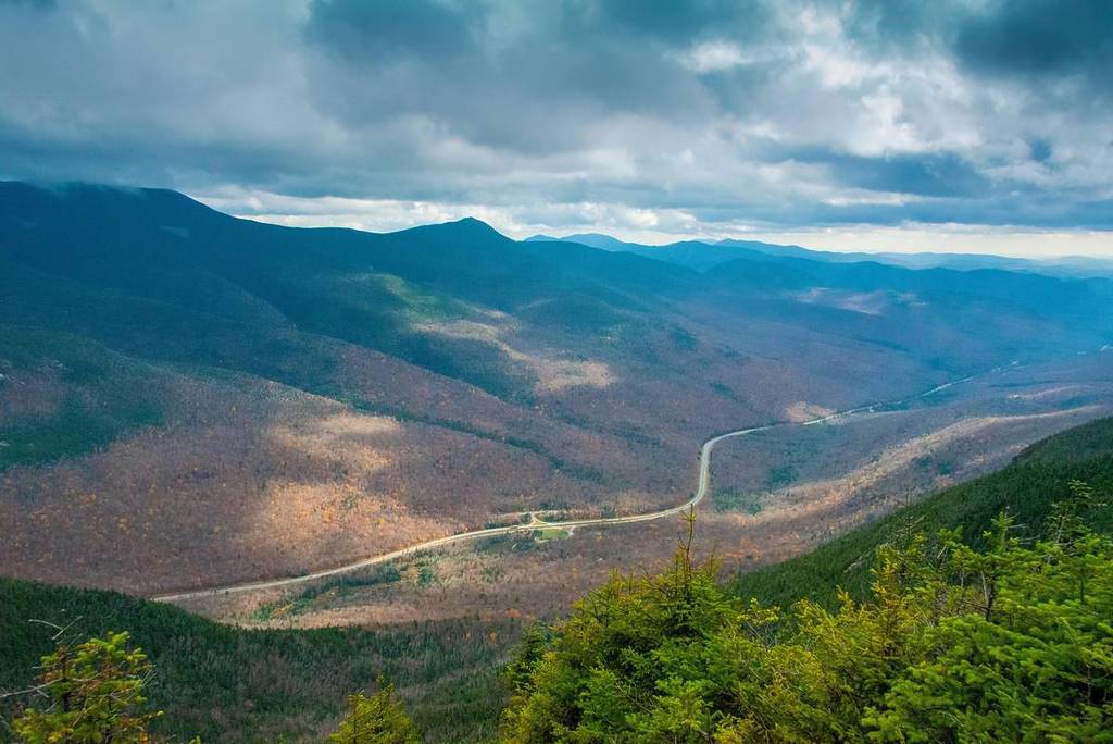 Stunning panoramic view of White Mountains, NH, showcasing the vibrant fall foliage from atop a scenic overlook.

