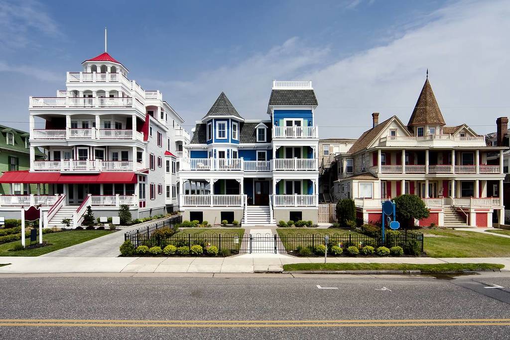 Colorful Victorian style houses alongside a road. Beautiful wooden homes with balconies and porches, painted red, blue, white and orange, under a blue summer spring sky, in Cape May, NJ. 