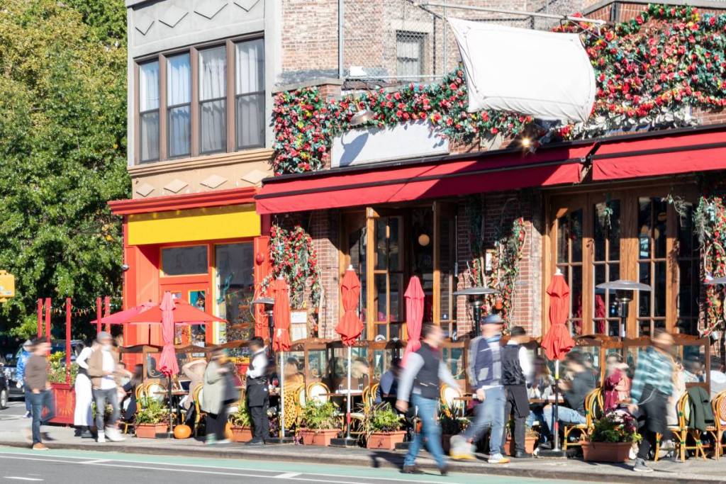 Cena movimentada de rua com multidões de pessoas em restaurantes com mesas ao ar livre na 7ª Avenida, no West Village, em Nova York (NYC)