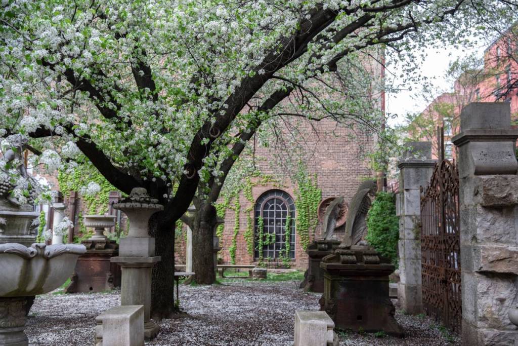 Red brick building covered in ivy with ornamental columns and figures in Elizabeth Street Garden in Nolita, Manhattan