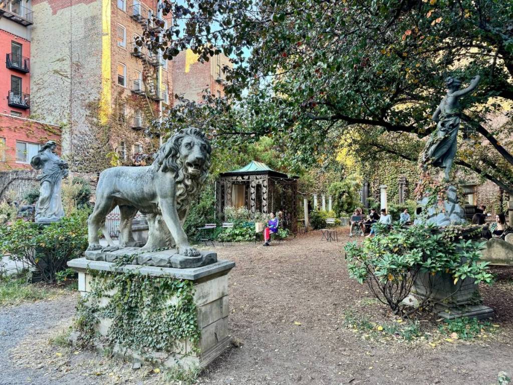 People sitting around the sculptures in the Elizabeth Street Garden on a fall day in Nolita, Manhattan, New York City