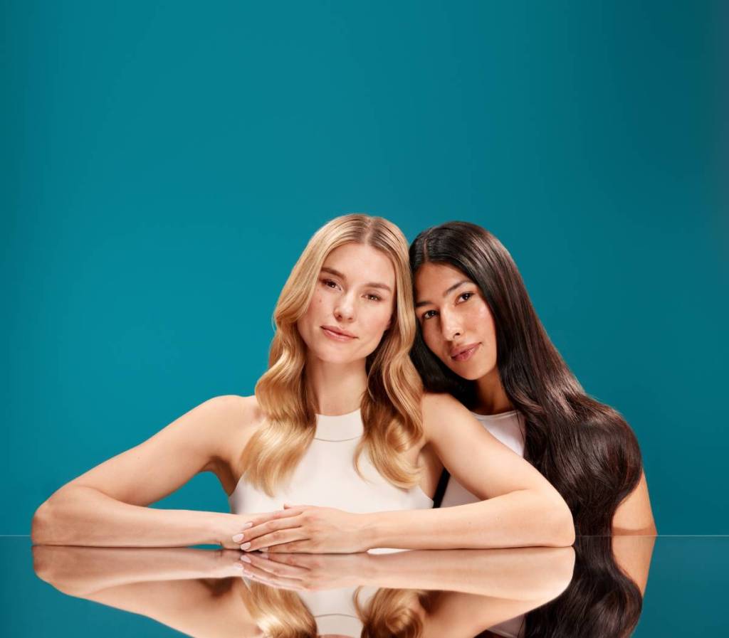 a blonde woman and brunette with glossy hair pose to showcase OGX repair range 