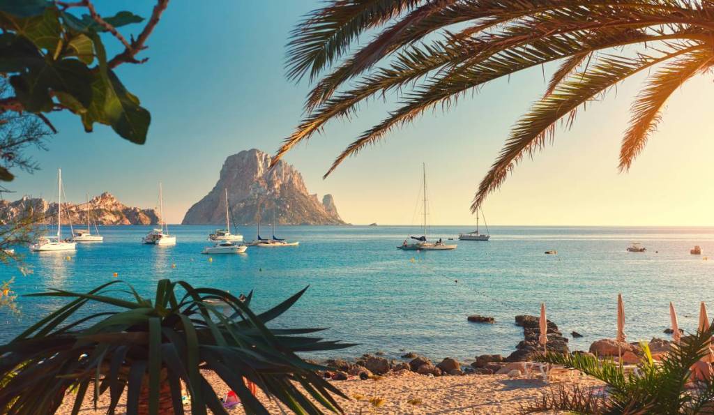 Famous, empty and beautiful Cala d'Hort beach, in summer very popular, sandy coast have a fantastic view of mysterious island of Es Vedra. Moored vessels on bay. Ibiza Island, Balearic Islands. Spain