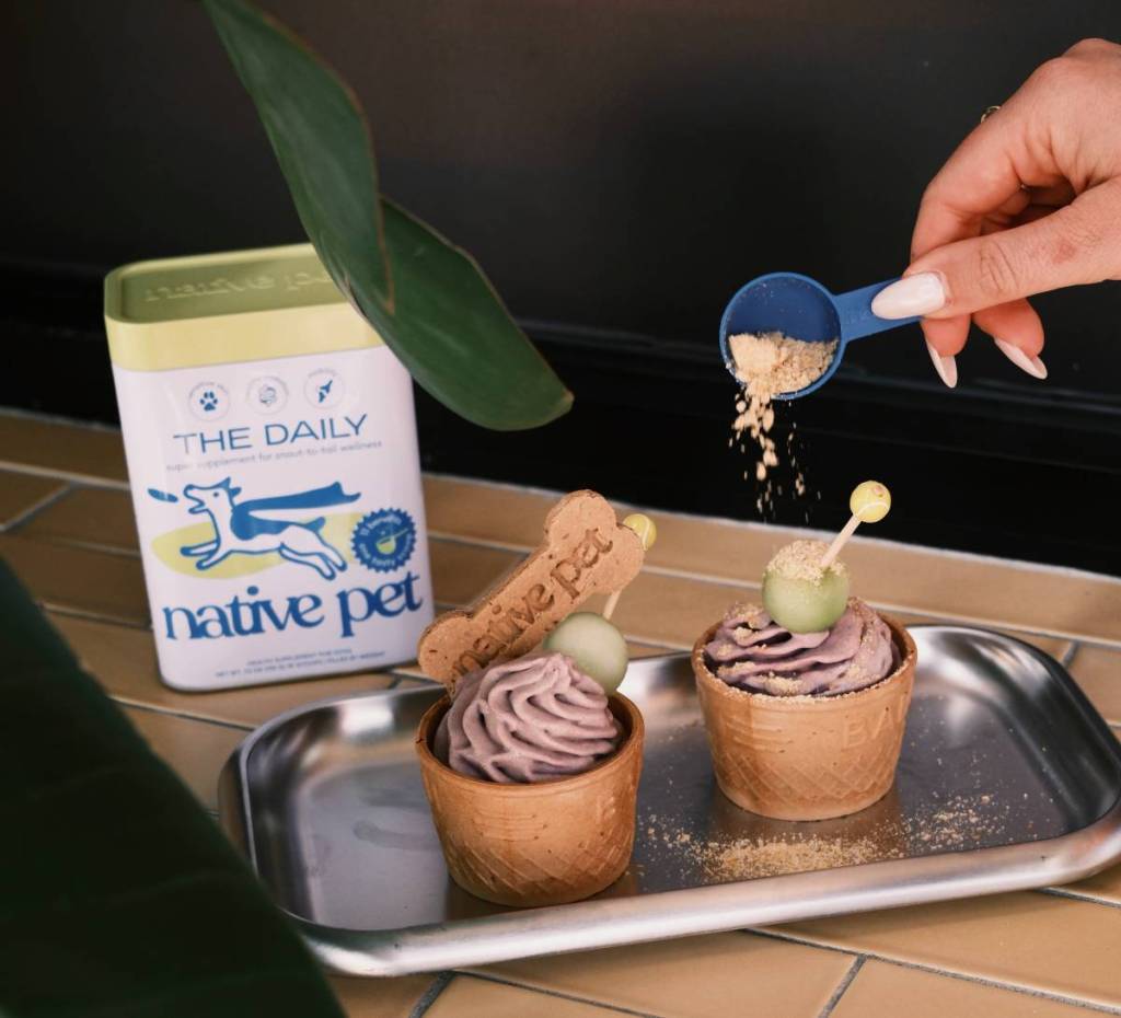 native pet 'double deuce' pup cups on a tray with a hand sprinkling native pet supplements over them