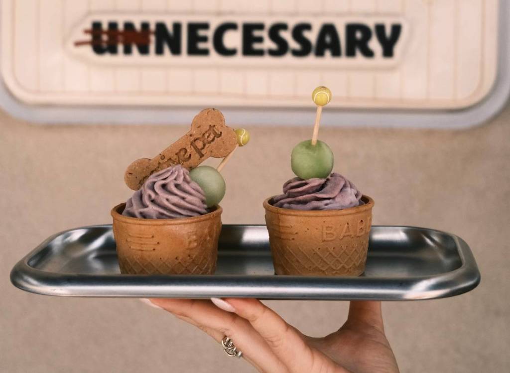 two native pet daily deuce pup cups held up on a silver tray, showing the pop-up venue Unnecessary NYC  sign on the wall behind 
