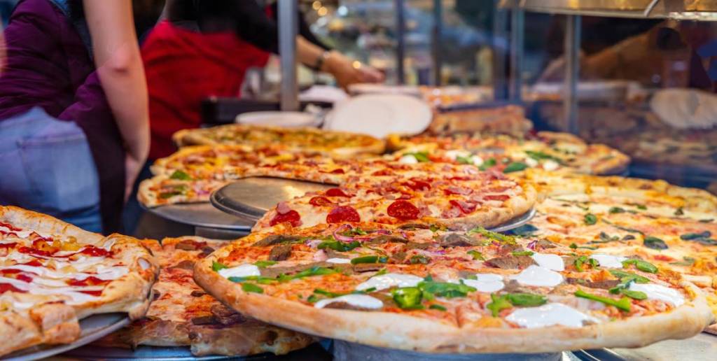 Glasvitrine einer Pizzeria. Verschiedene italienische Pizzen in der Auslage, Streetfood. Küchenmitarbeiter, die die Pizzen anrichten