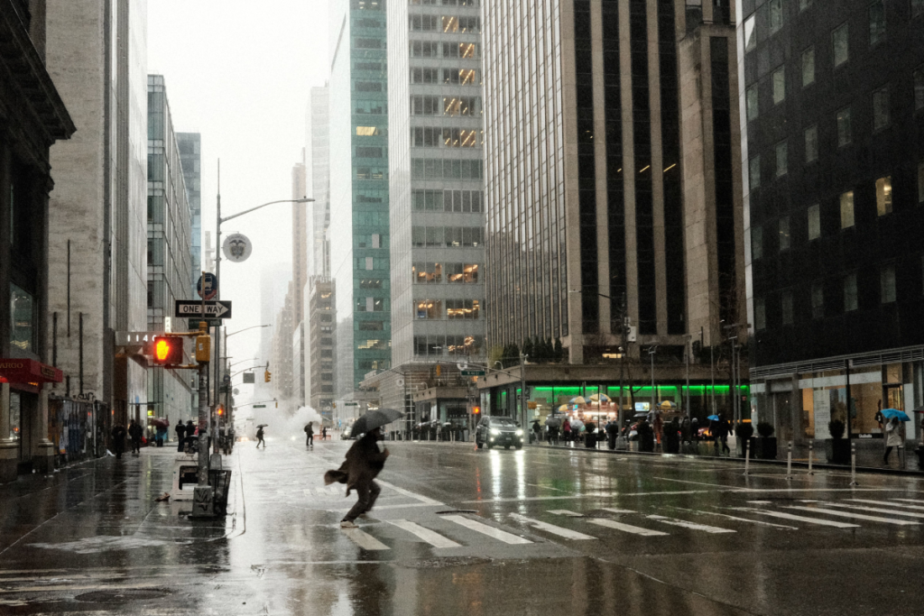 Escena callejera en Nueva York con gente y paraguas bajo la lluvia, que refleja la vida urbana