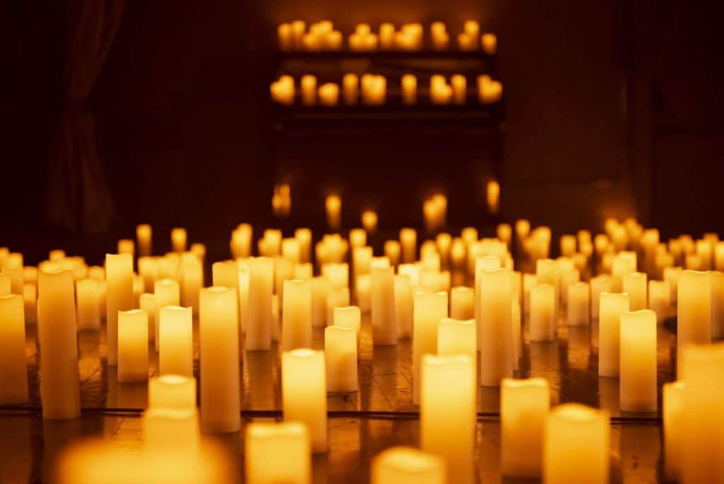 A close-up of candles with more candles visible at a height in the background.