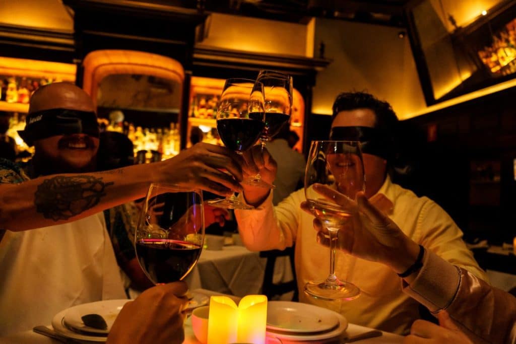 A group of guests clink glasses whilst blindfolded.