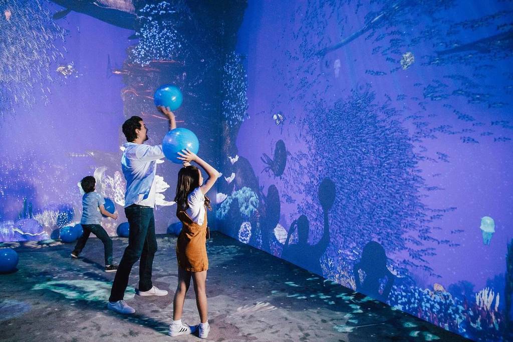 A father and his son and daughter throw balls at the walls of the interactive virtual aquarium at Dinos Alive.