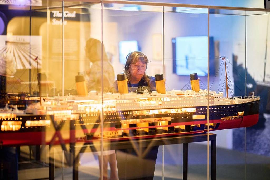 A woman wearing a headset stares at a model of the Titanic in a glass case at Titanic. The Human Story.