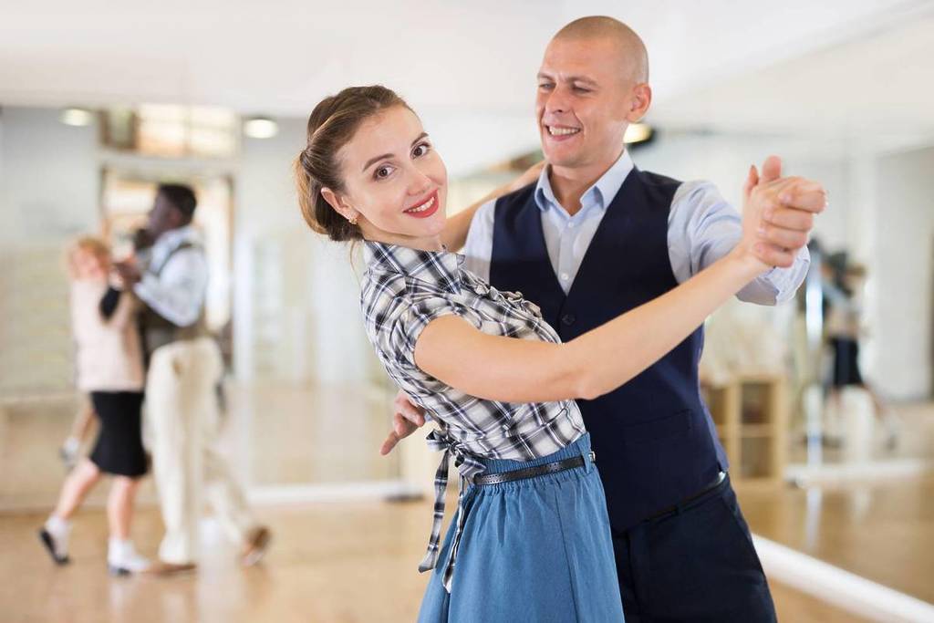 The image shows a couple ballroom dancing with the woman looking directly into the camera while the man looks at her.