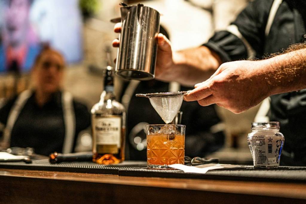 A bartender pours a cocktail into a glass at a speakeasy.
