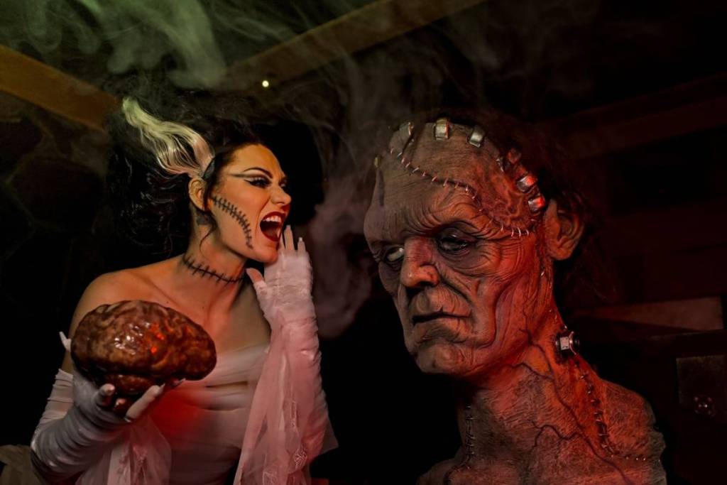 A woman holds a brain in her hands and speaks into the ear of Frankenstein's monster at Escape This.