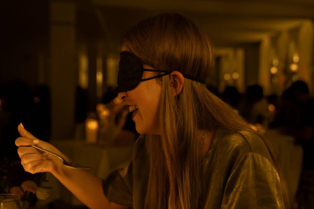 A woman smiling and trying a spoonful of food at Dining in the Dark.
