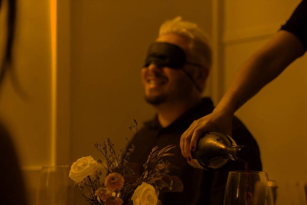 A man smiling while wine is being poured at Dining in the Dark.