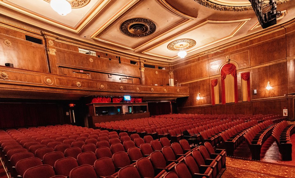 The auditorium of the Media Theatre featuring grand chandeliers, red-velvet seats, and a majestic proscenium stage
